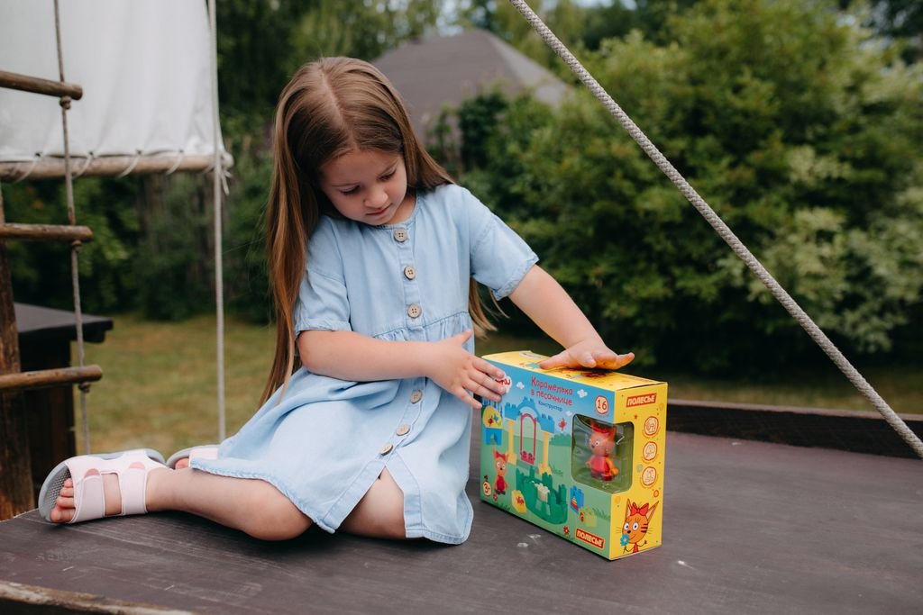 A girl enjoys a sunny day outdoors, playing with a colorful toy on a wooden structure.