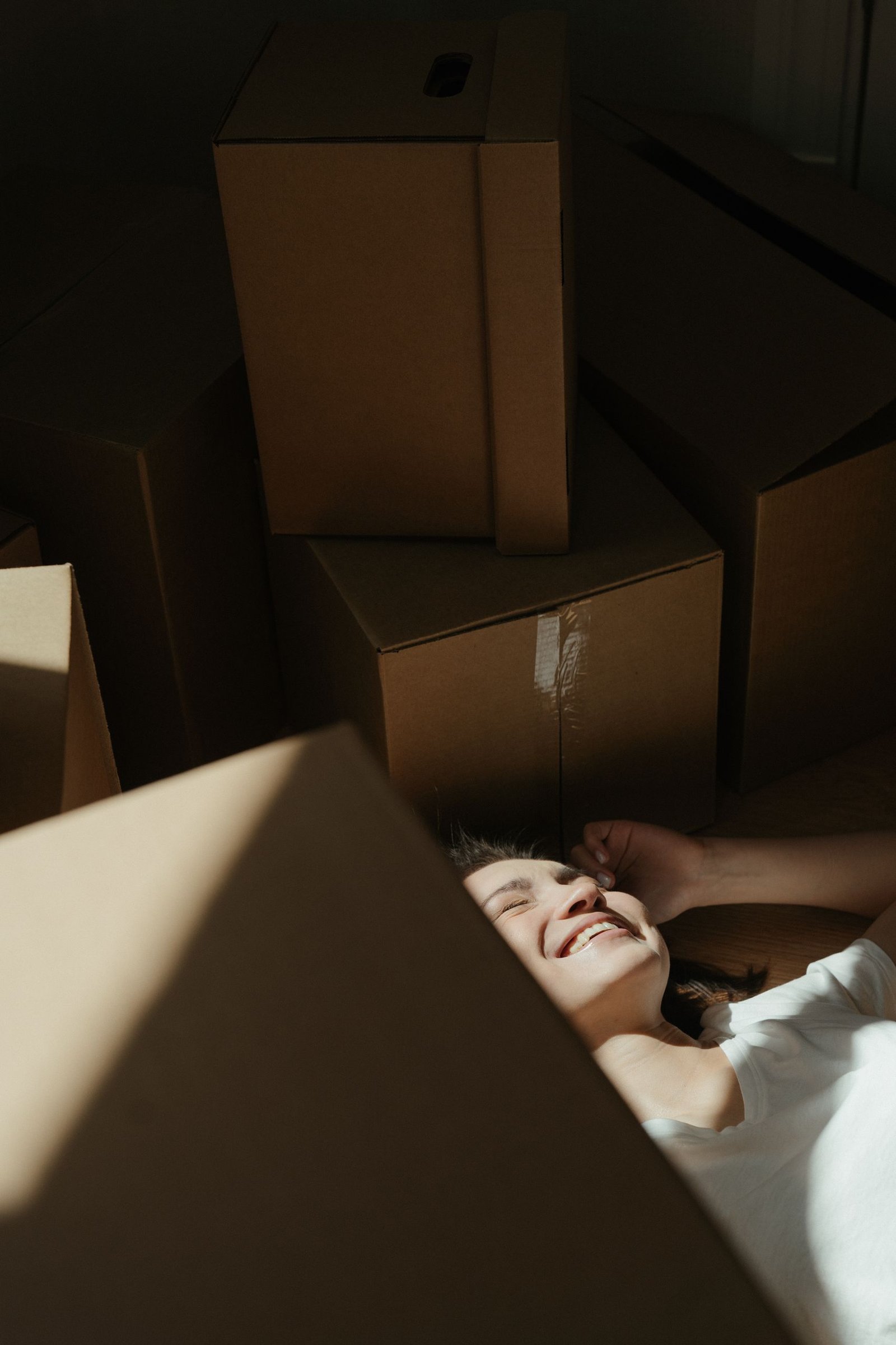 A joyful woman smiles surrounded by cardboard boxes, symbolizing a new beginning.