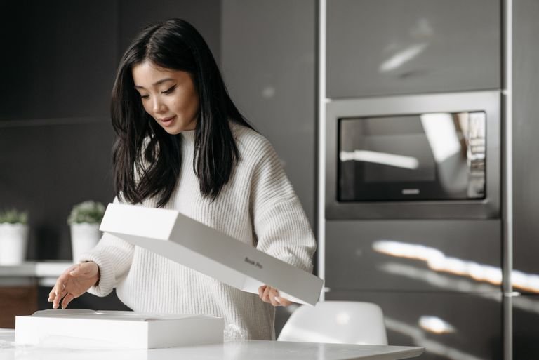 An asian woman excitedly unpacks a delivery box in her modern kitchen.