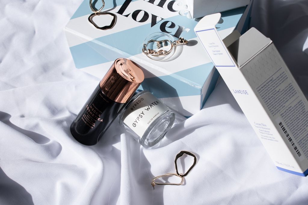 Chic arrangement of skincare bottles and jewelry on white fabric, highlighting luxury beauty products.