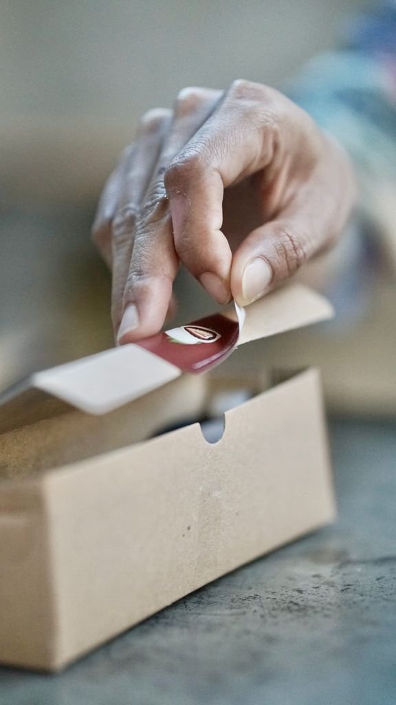 Close-up of a hand sealing a cardboard box with a sticker, showcasing packaging process.