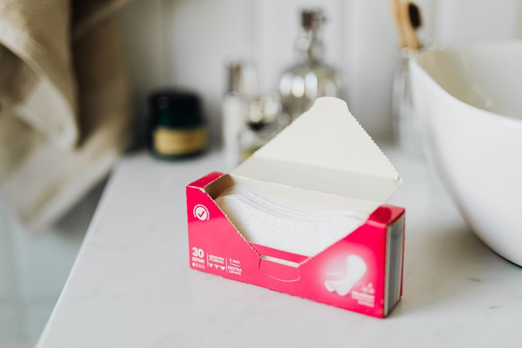 From above of open package of sanitary napkins placed on white surface near ceramic sink in modern bathroom