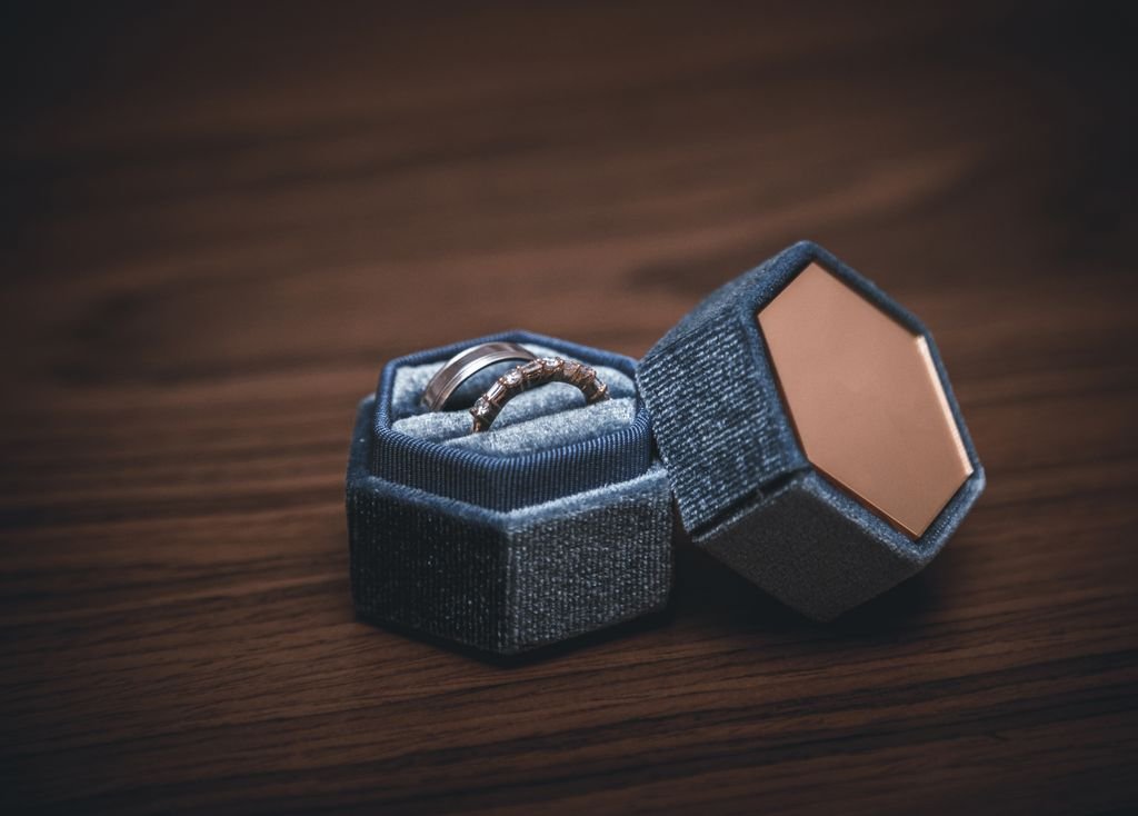 Luxurious engagement and wedding rings elegantly displayed in a blue velvet hexagonal box on a wooden surface.
