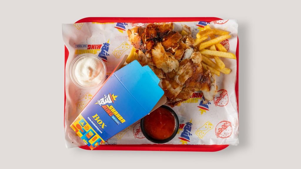 Mouth-watering shawarma platter with fries on a tray, including dipping sauces and vibrant packaging.