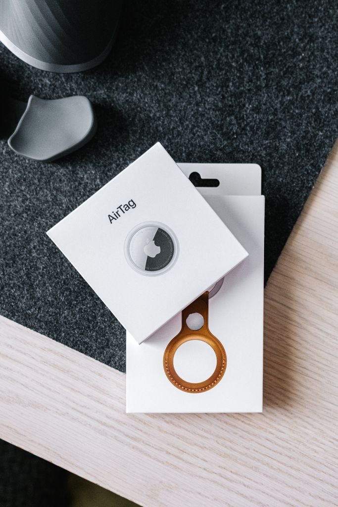 Overhead shot of AirTag and leather key ring packaging on wooden surface.