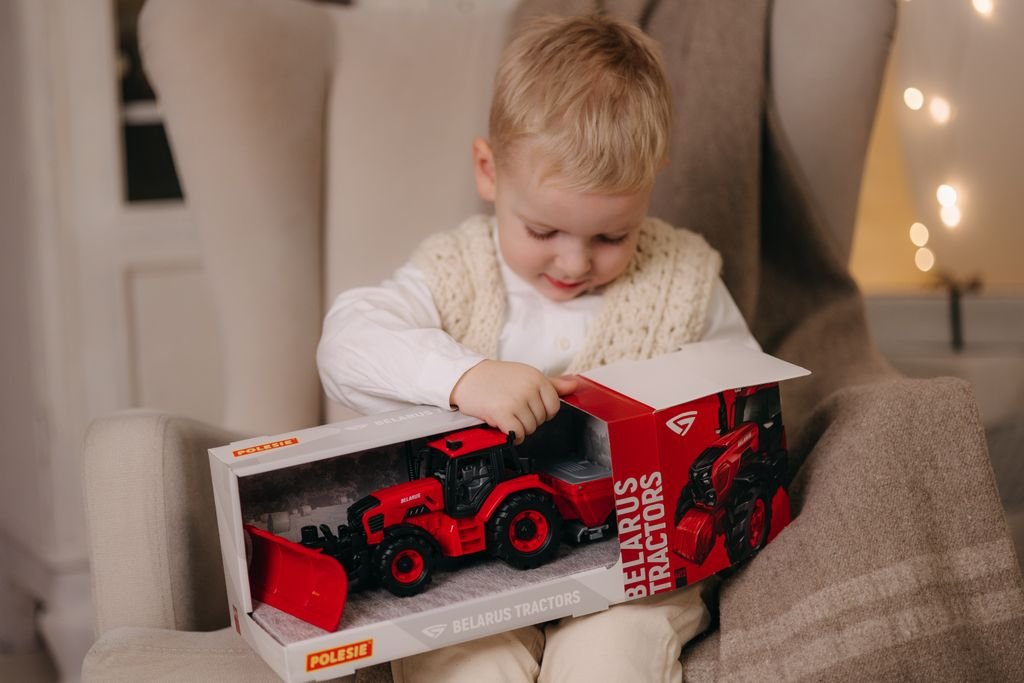 Young child excitedly opens a toy tractor gift indoors during Christmas celebrations.